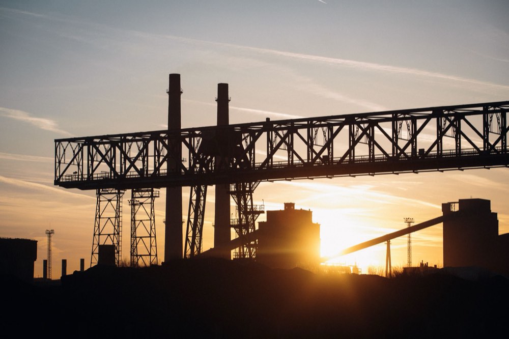 Site industriel au coucher du soleil : portiques, cheminées et lignes électriques